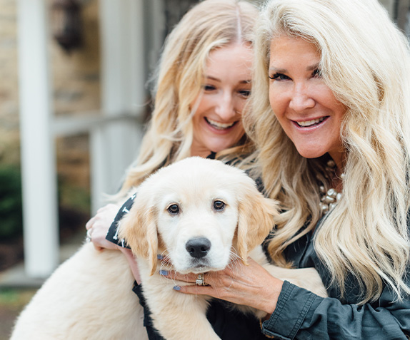 Anne and Meghan Townes Smiling with a Small Golden Retriever Puppy